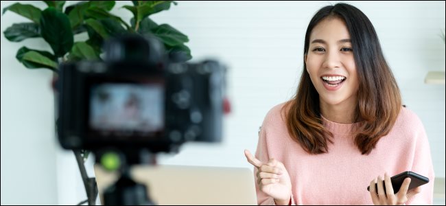 A woman filming a video on a camera in front of a laptop.