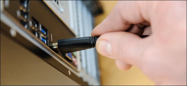 A hand plugging an HDMI cable into a desktop PC.