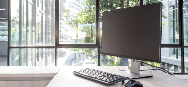A desktop computer monitor, keyboard, and mouse on a desk.
