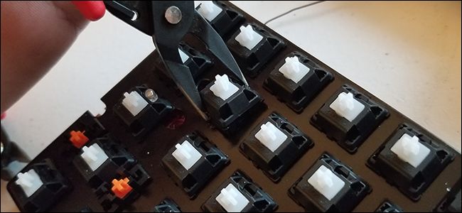 Someone pulling a key switch mechanism out of a keyboard with some pliers.