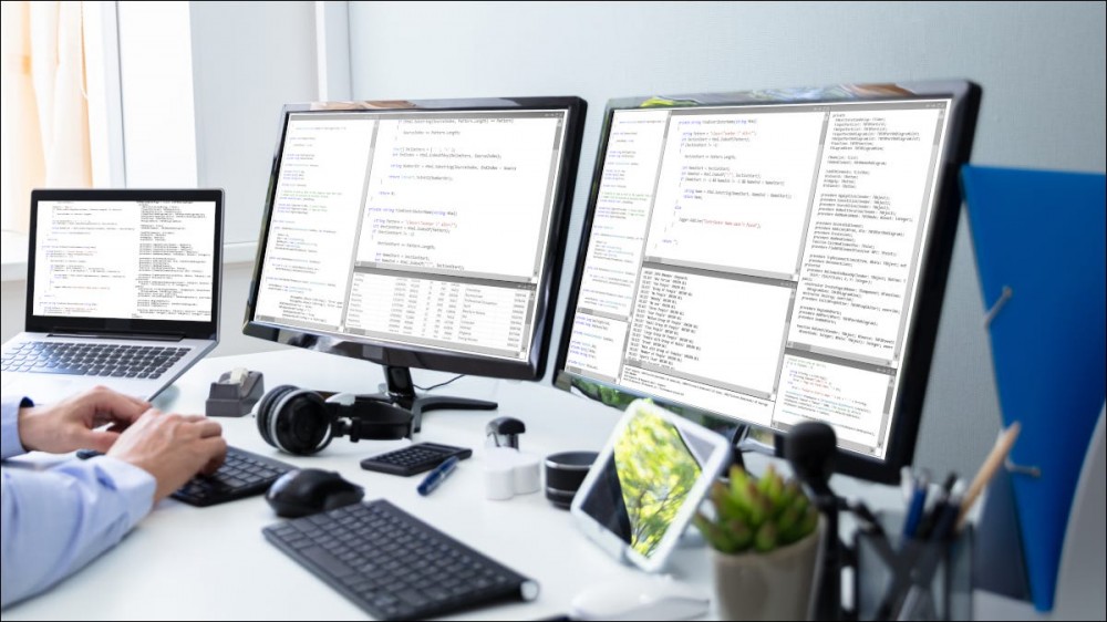 Dual monitors set up next to a laptop on a home computer desk.